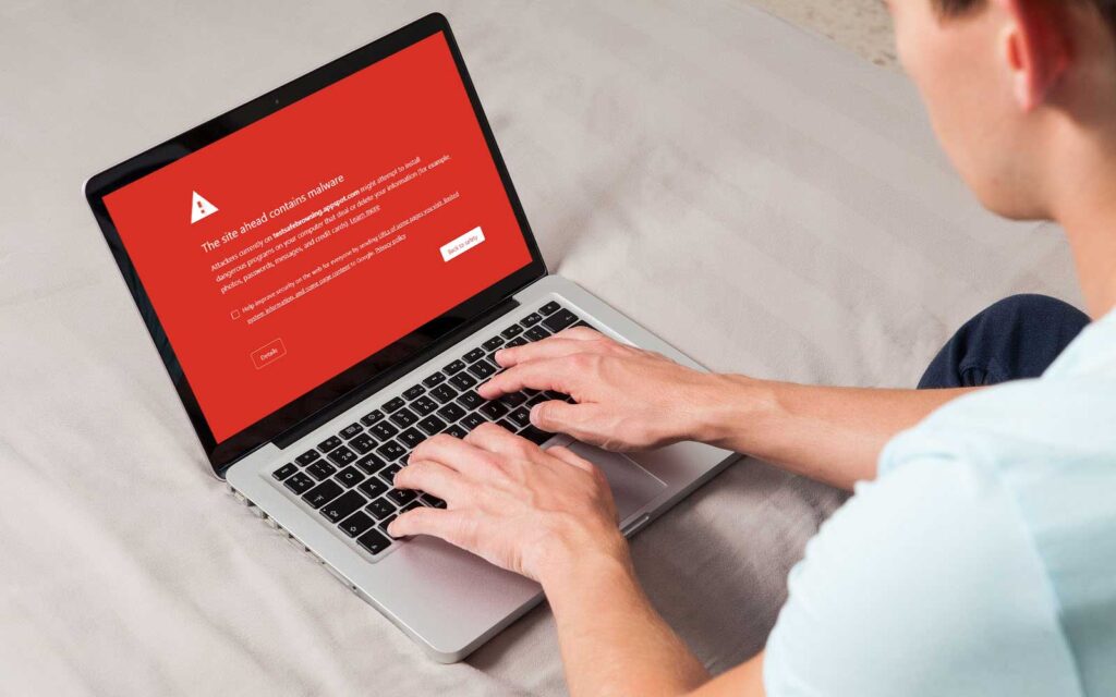 Person using a laptop displaying a red malware warning, illustrating the risk of visiting a suspicious or reused file-sharing domain.